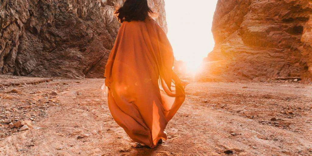 a woman in an orange dress walking through a canyon